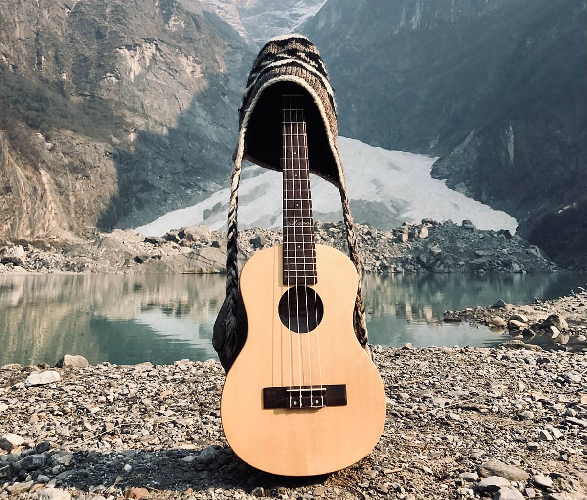 guitare acoustique marron sur un quai en bois marron près d'un lac et d'une montagne couverte de neige pendant la journée